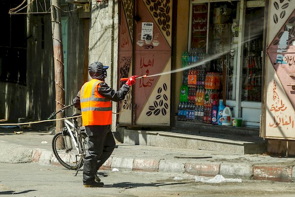 أحد الطواقم الصحية يقوم بتعقيم واجهة دكانة في مدينة غزة 